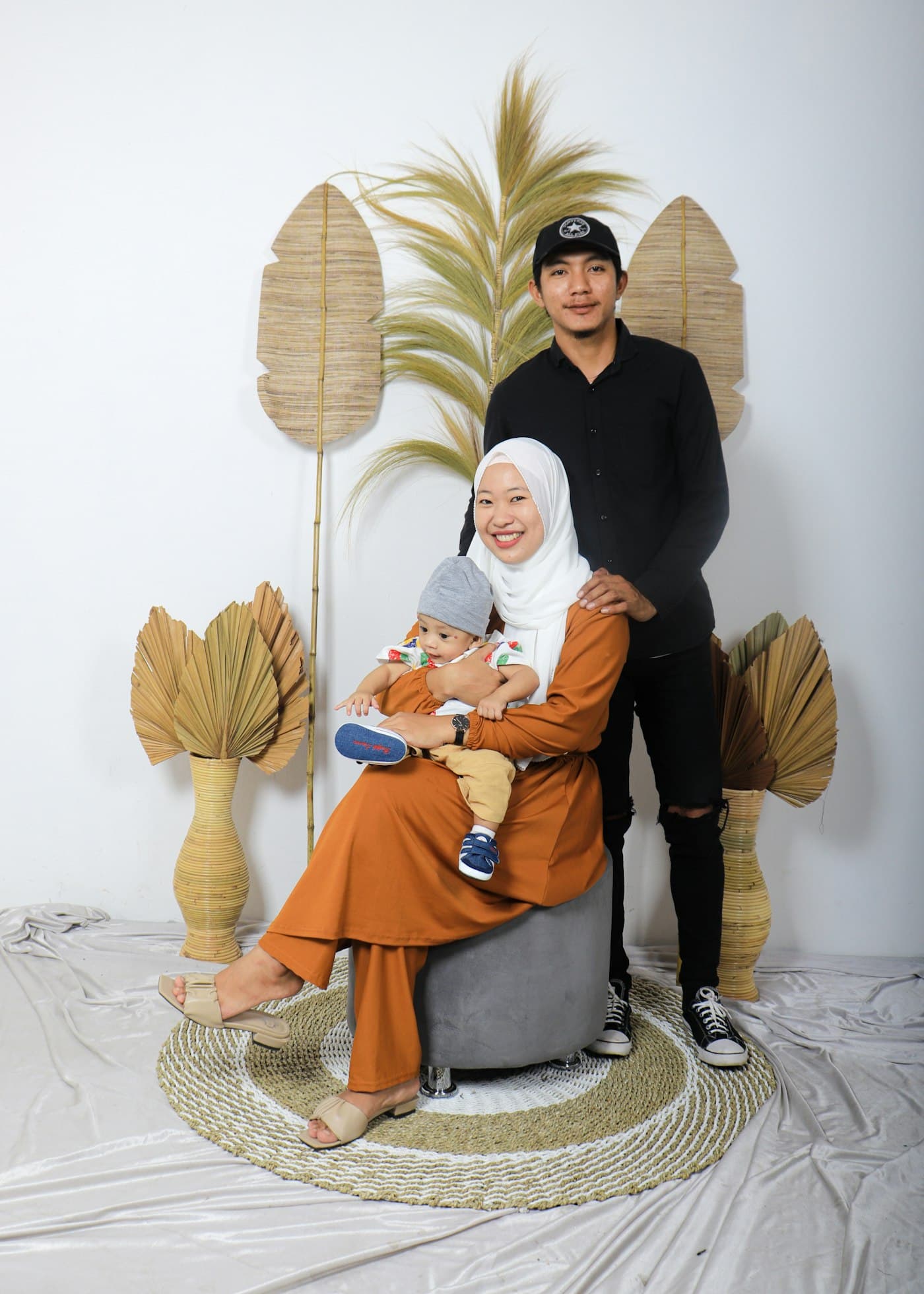 Keluarga dengan ibu berhijab menggendong bayi di set berdekorasi daun kering