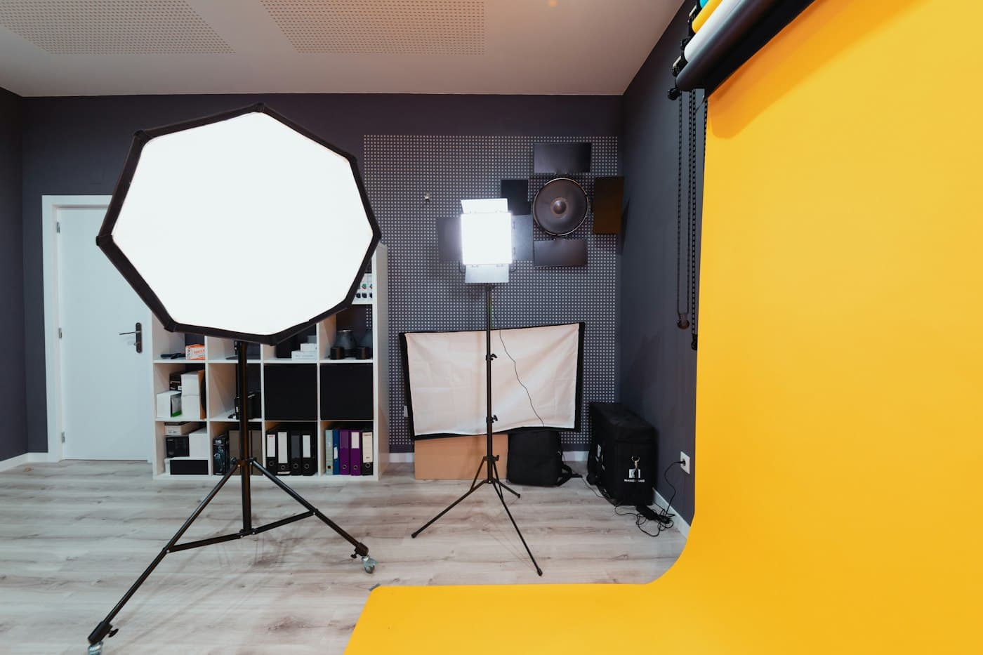 Studio dengan lantai kuning, softbox, lampu LED, dan rak perlengkapan