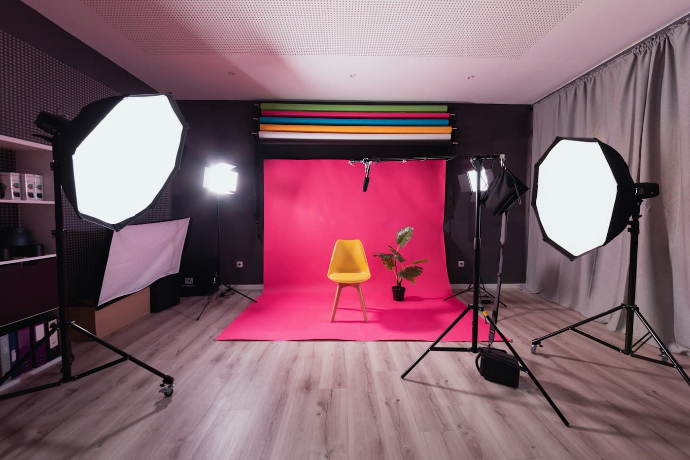 Studio dengan latar magenta, kursi kuning, tanaman, dan lampu studio